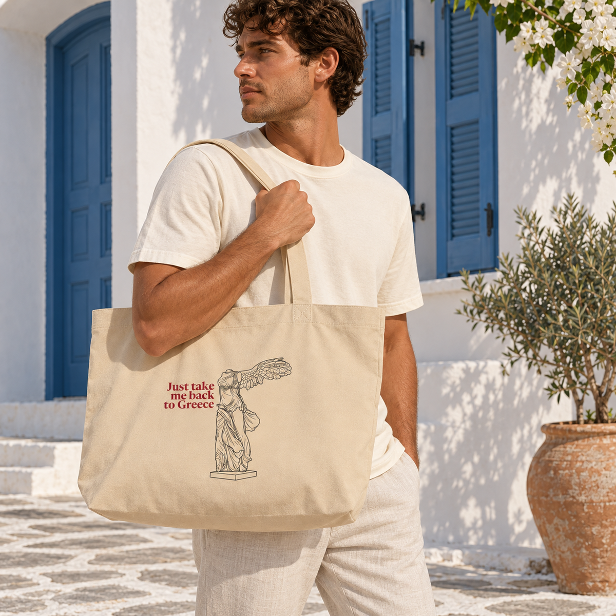 Lifestyle mockup: man carrying the Large Oyster Winged Victory organic cotton tote in a sunlit Greek courtyard