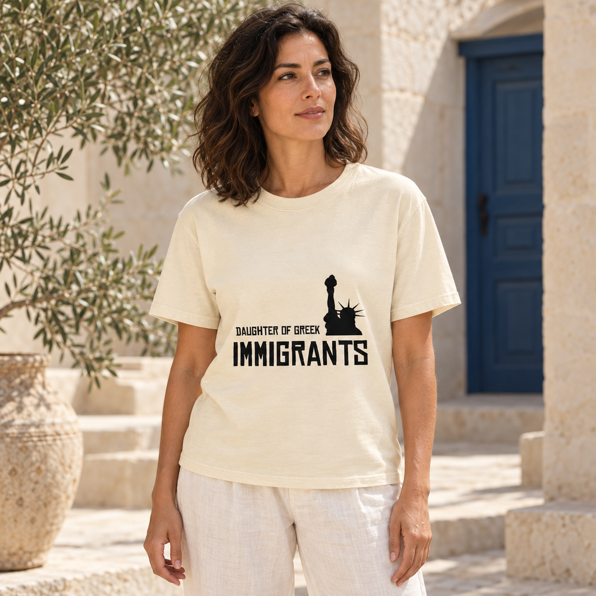 Daughter of Greek Immigrants — USA — Ivory shirt worn by a model in a sunlit stone courtyard; AI-generated lifestyle mockup