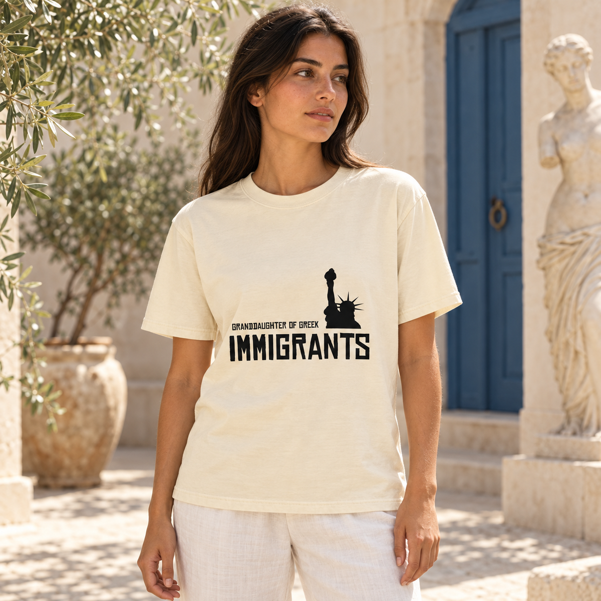 Granddaughter of Greek Immigrants — USA — Ivory shirt worn by a model in a sunlit stone courtyard; AI-generated lifestyle mockup